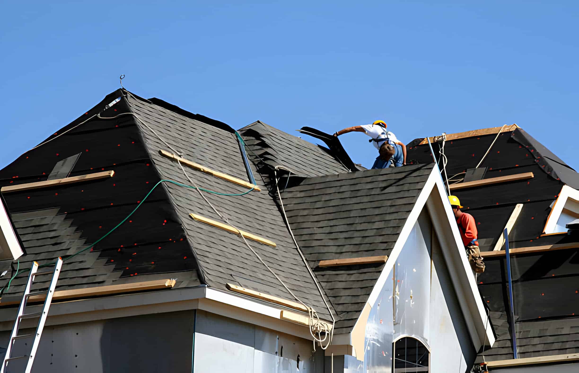 Construction workers installing shingles on the roof of a home.